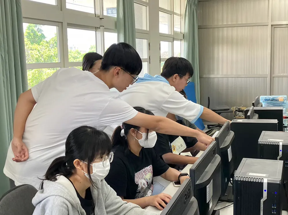 志工彎下腰，在電腦教室裡一對一指導孩子畫 3D 圖