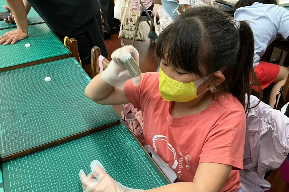 孩子戴著手套，舉起手上的玻璃瓶，觀察瓶壁形成的銀鏡