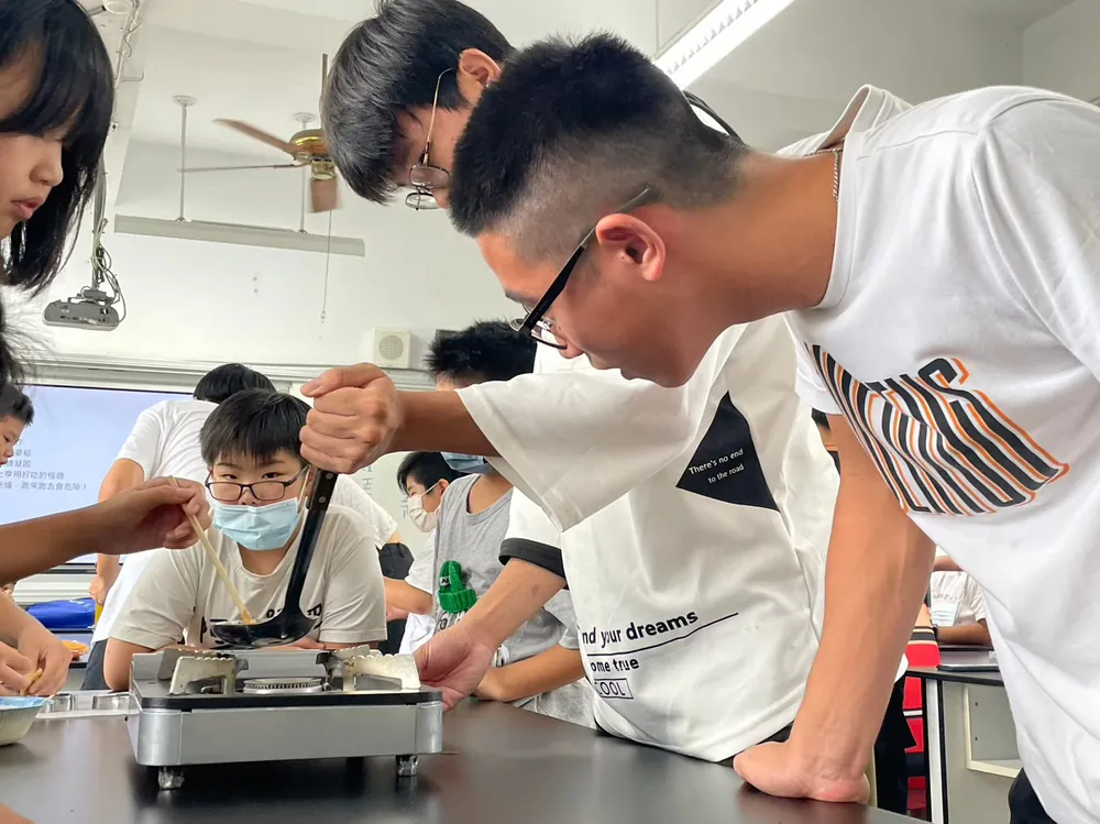志工俯身在爐火上攪動糖漿，孩子們專心看著