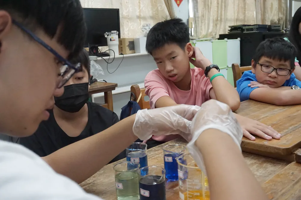 孩子們托著臉頰，看著桌上一杯杯藍色、綠色與橘色的液體