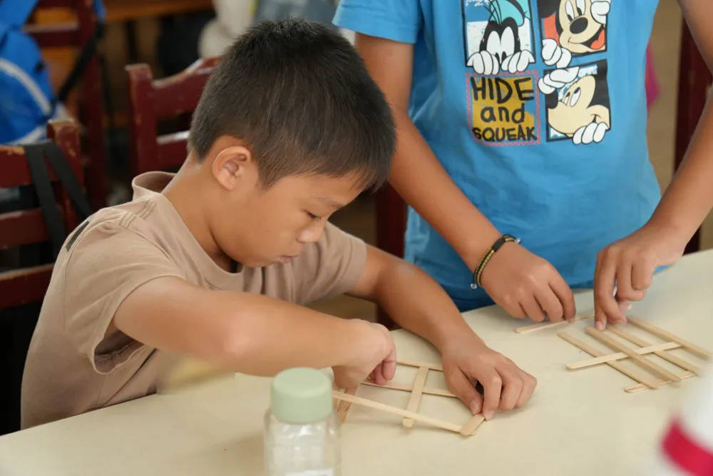 孩子低著頭專心地把木棍一根根交錯疊成橋