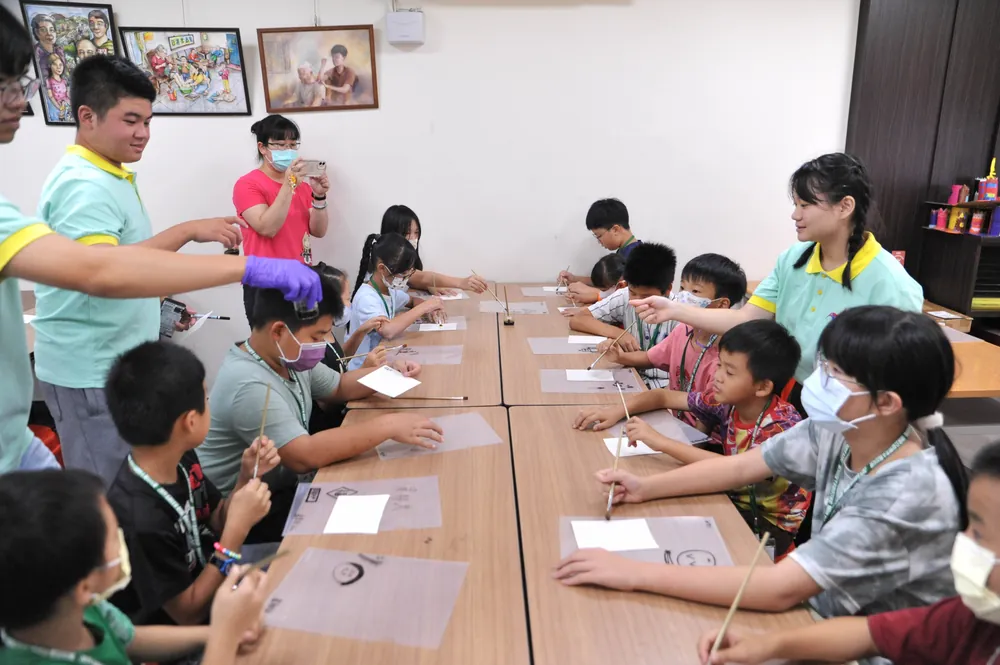 孩子們坐在長桌邊，在透明片上用水彩筆畫出自己的圖案